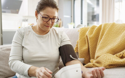 Mature woman sitting on sofa using digital blood pressure gauge to measure high blood pressure.